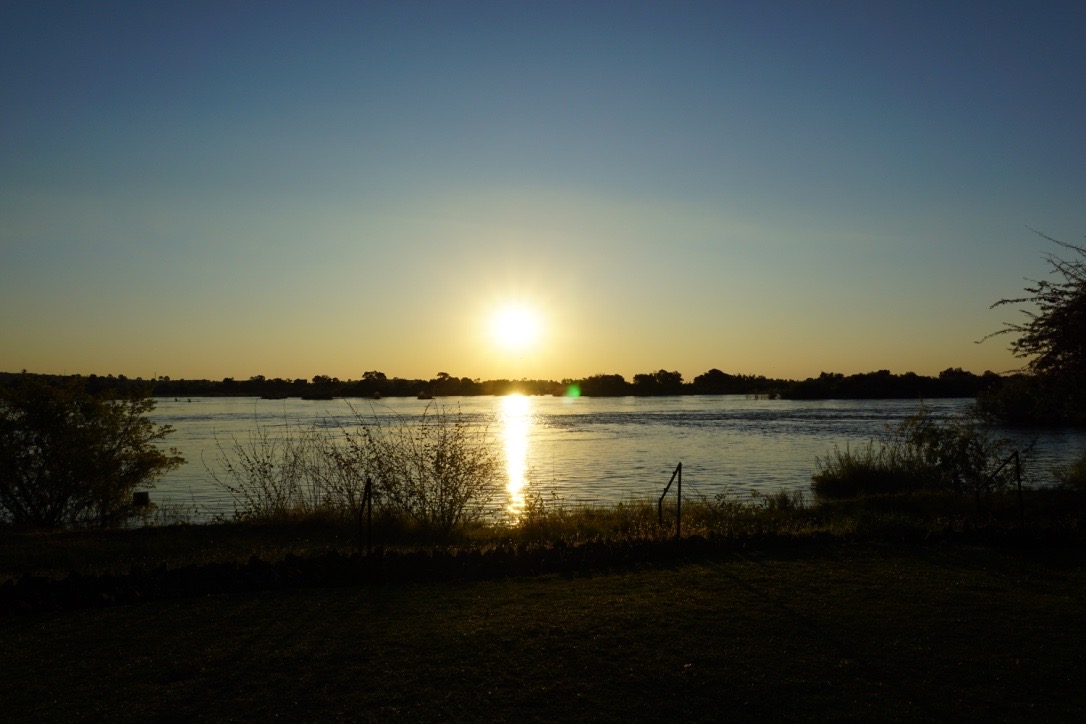 A sunset over the water with grass in front of it.